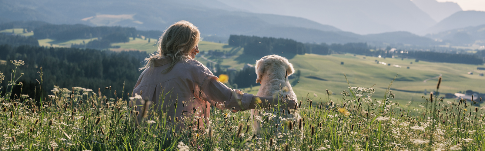 Katharina Miklauz sitzt mit Nala auf einer Wiese und sieht sich die Berge im Vorderung an