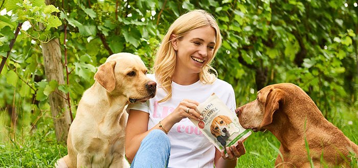 Katharina Miklauz siede tra le vigne e nutre i cani Enzo e Pluto con i nostri snack DOG'S LOVE